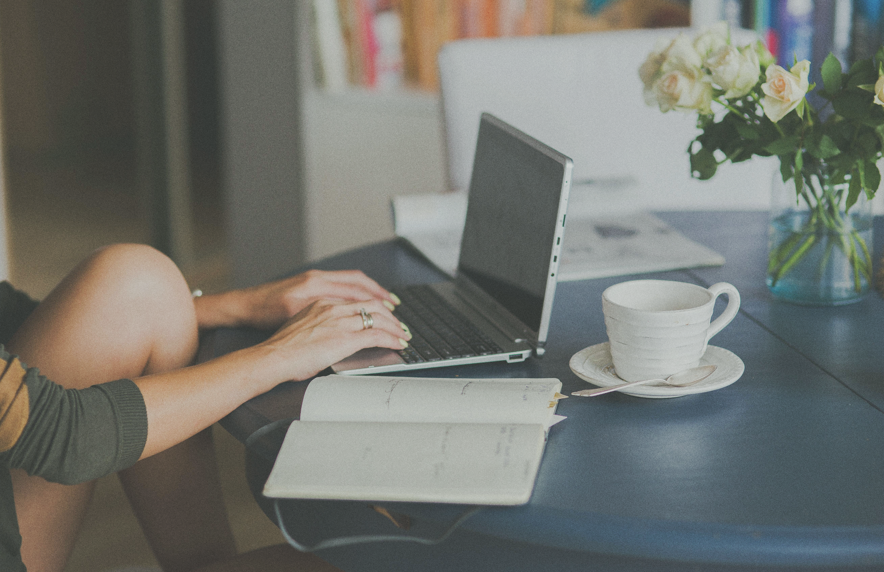 person typing on laptop with open notebook on the table